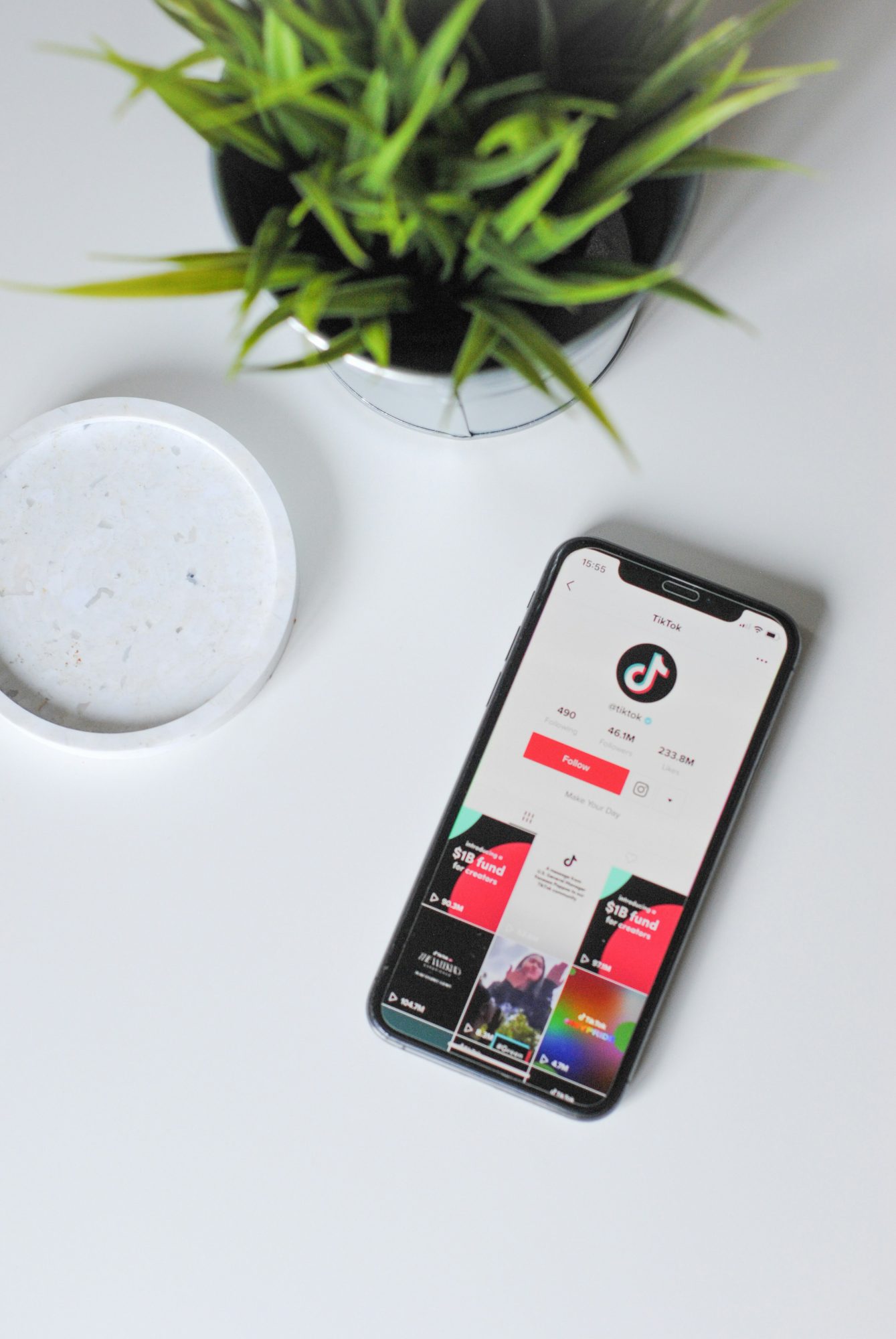 Smartphone cu aplicatia TikTok deschisa pe o masa alba, alaturi de o planta si un suport pentru cana – imagine reprezentativa pentru strategii moderne de social media marketing, ilustrand platforme populare pentru continut organic si reclame.